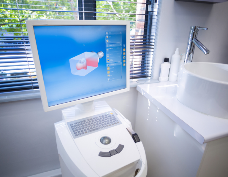 A close-up of a dental CAD/CAM machine displaying a 3D model of a tooth on its screen. The high-tech equipment is used for designing and fabricating dental restorations in a modern dental office.